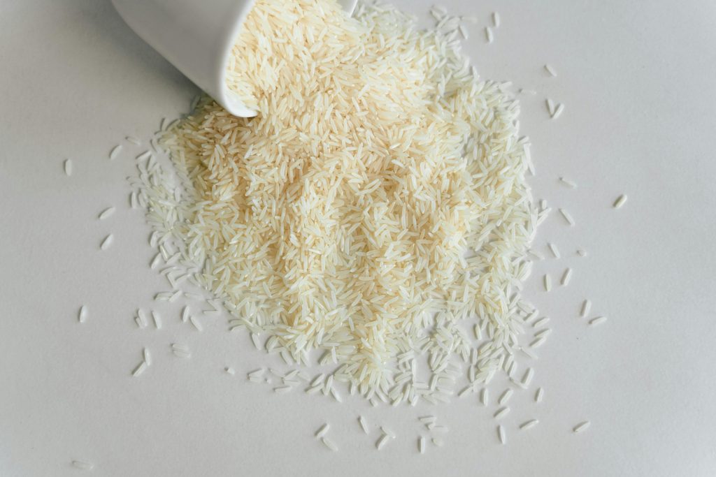 High-angle shot of uncooked white rice spilling from a ceramic cup onto a smooth surface.