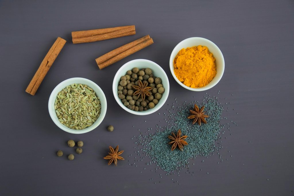 Flat lay of assorted spices including cinnamon, turmeric, and star anise on a dark surface.